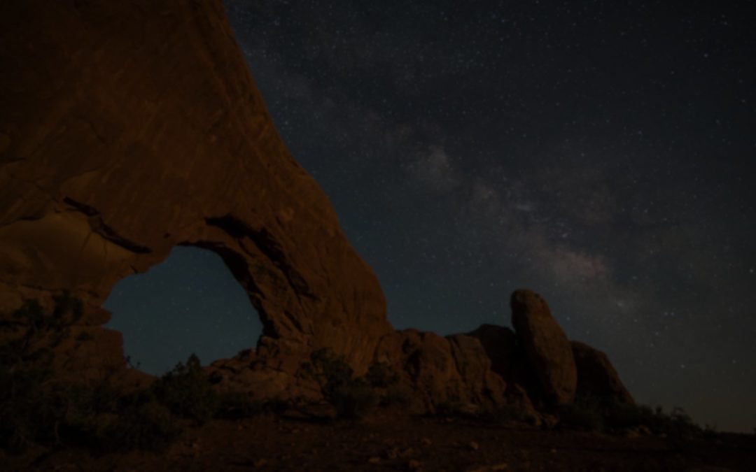 Night sky over a natural rock arch in a desert landscape.