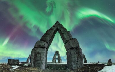 Northern lights over stone archway, snowy landscape.